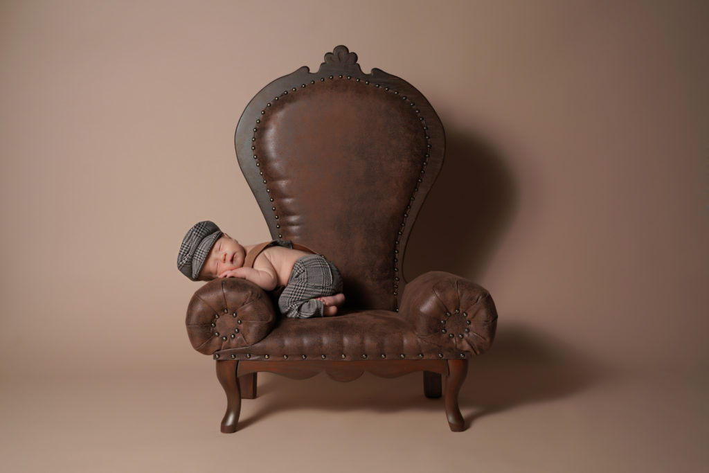 Newborn portrait of a baby sitting on the arm of a leather chair. Winter Park FL.