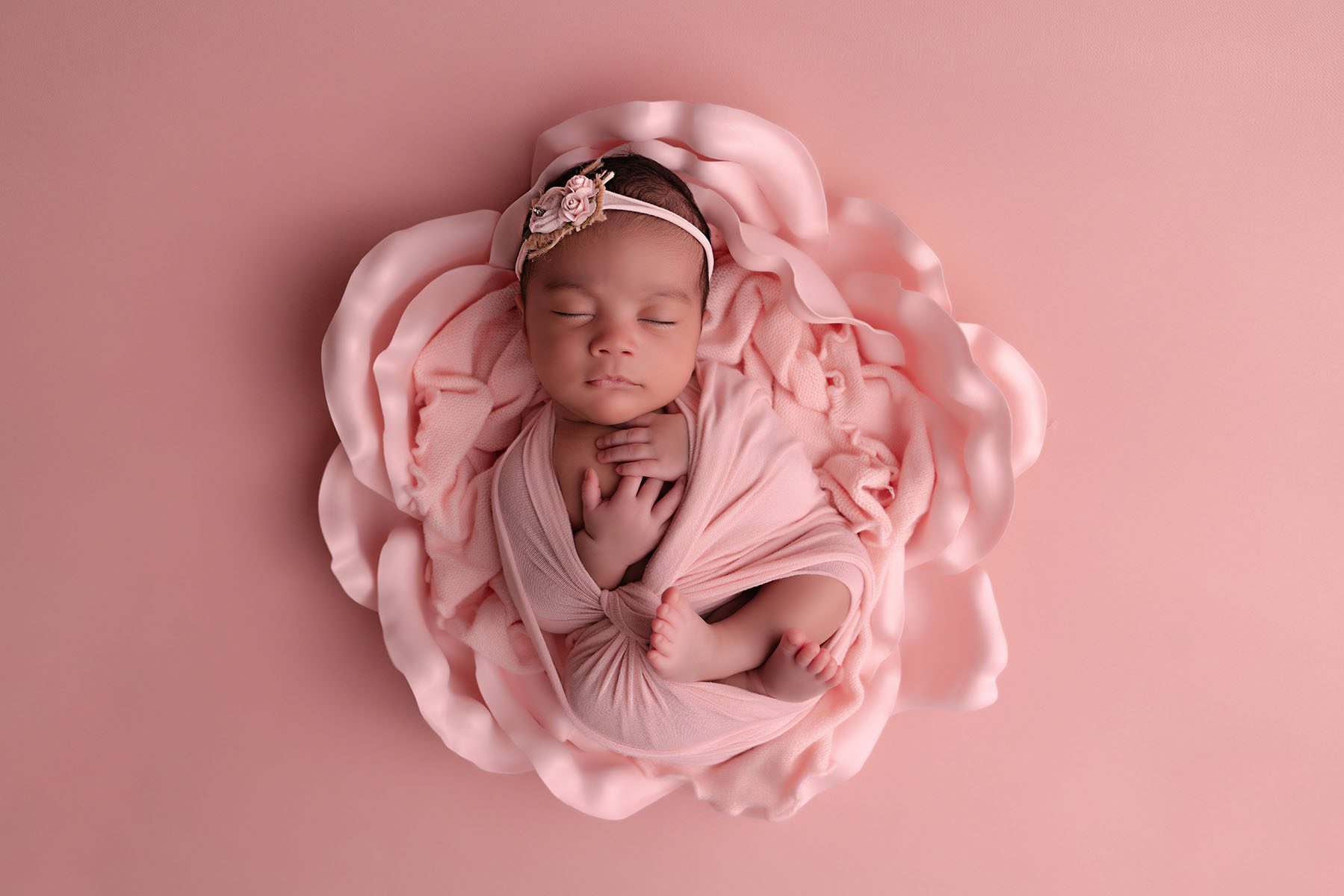 Floral themed newborn portrait of a baby wrapped in pink fabric laying on a flower prop