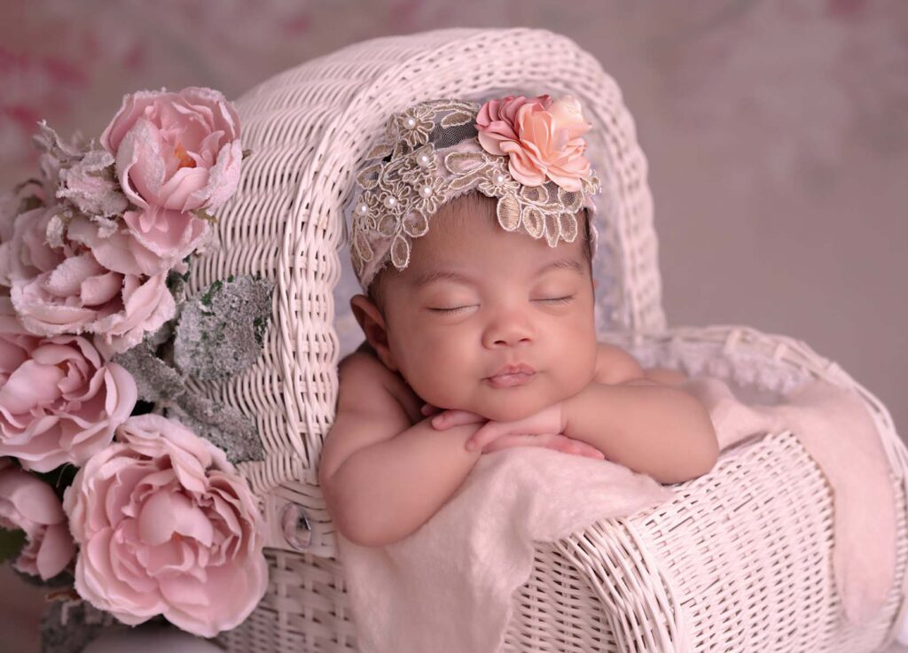 Portrait of newborn girl sleeping in a stroller prop in a pink photography set with flowers