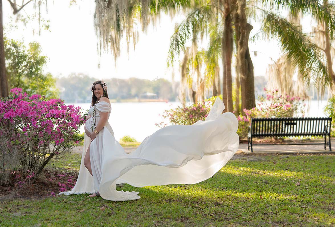 Maternity portrait of woman in a garden wearing a flowing white gown and flower crown