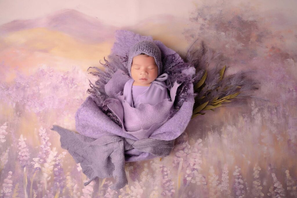Stylized newborn portrait of baby wrapped in purple fabric on a natural purple hued backdrop