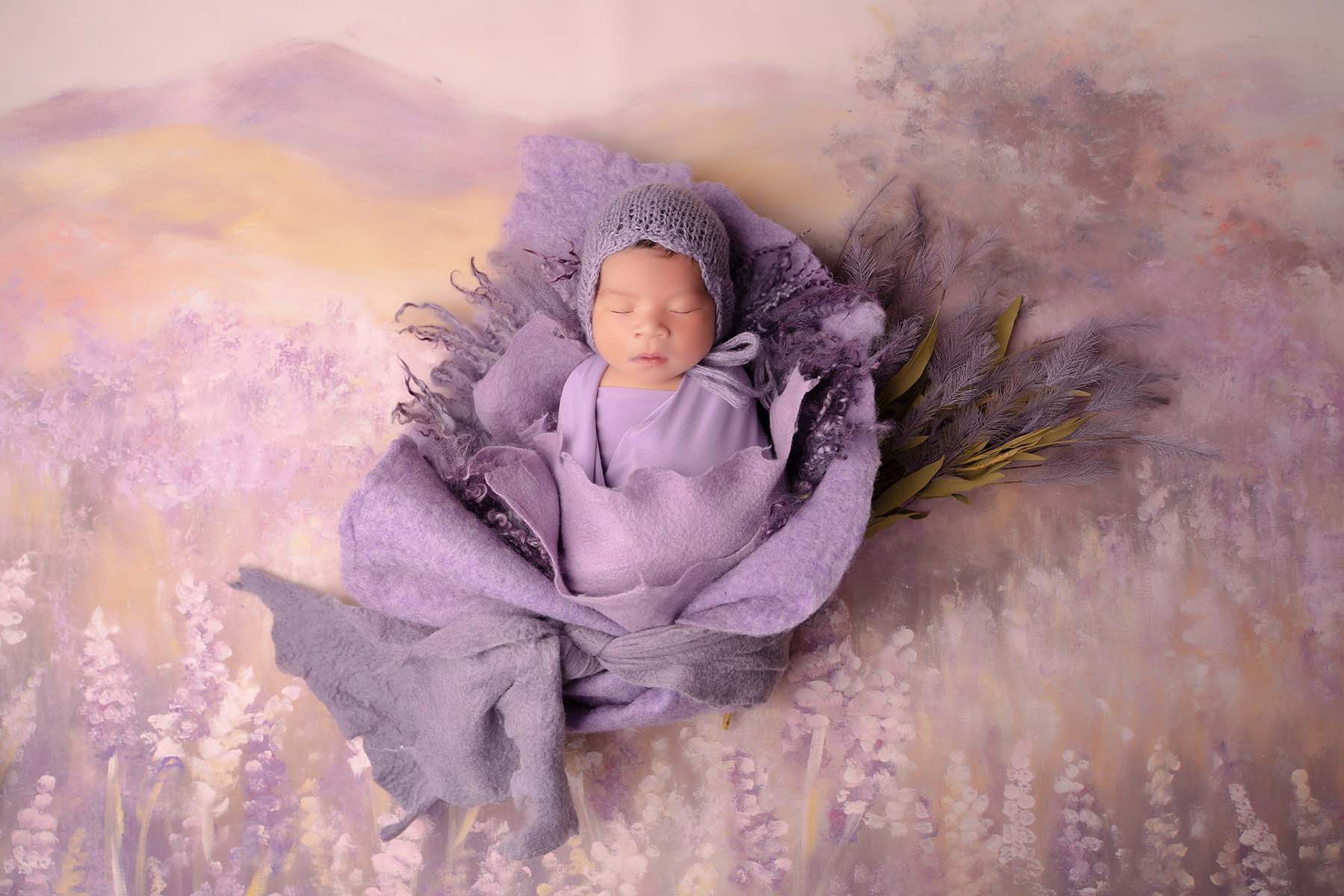 Stylized newborn portrait of baby wrapped in purple fabric on a natural purple hued backdrop