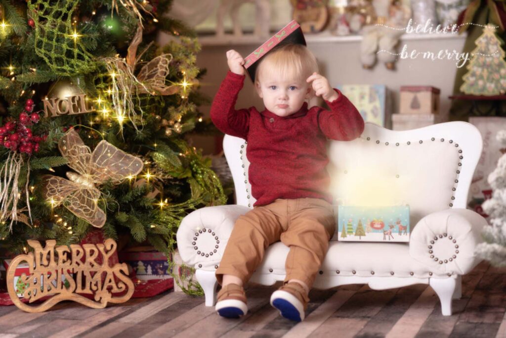 Portrait of a young boy in a christmas themed set holding a present box topper above his head