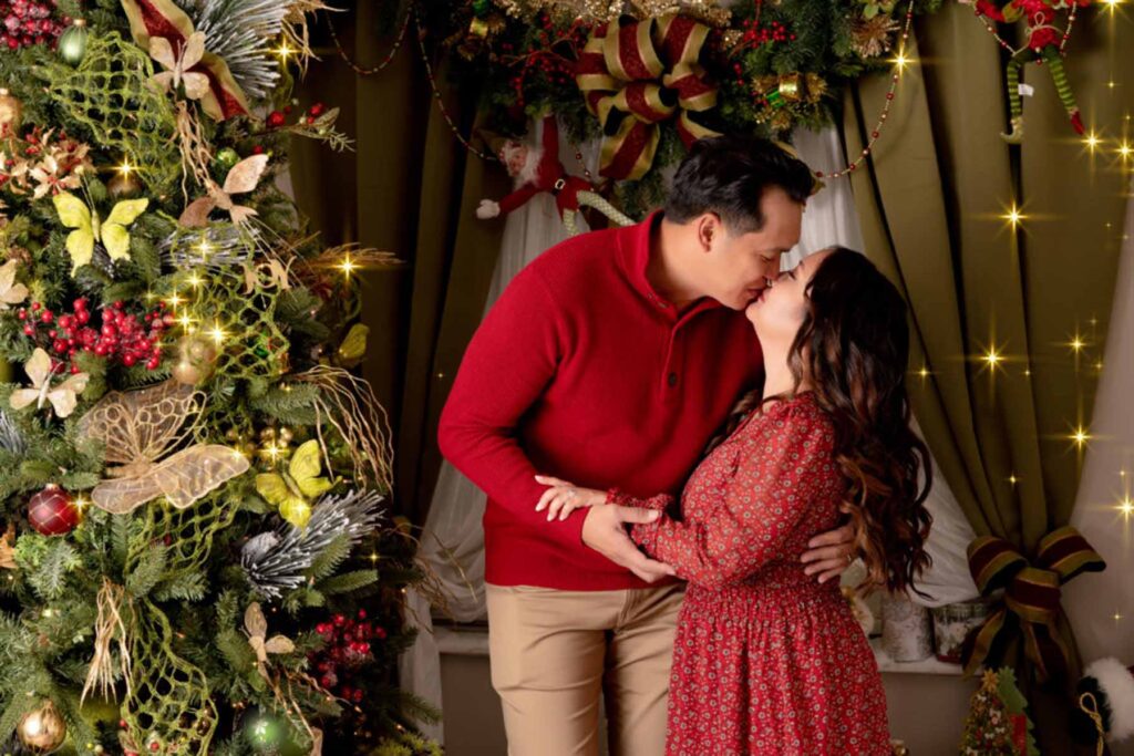 Christmas themed portrait of couple both in red posed in a christmas photography set