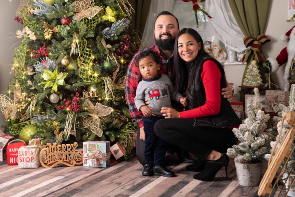Family christmas portrait of couple and their son posed next to a christmas tree