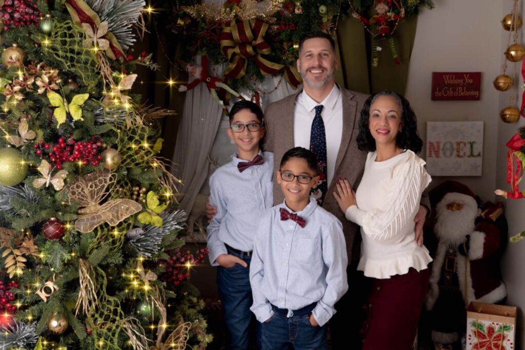 Christmas themed family portrait of a family posed beside a christmas tree
