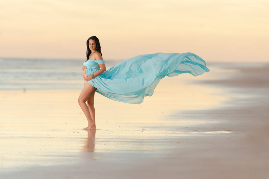Flying dress themed maternity portrait of woman posed on a beach