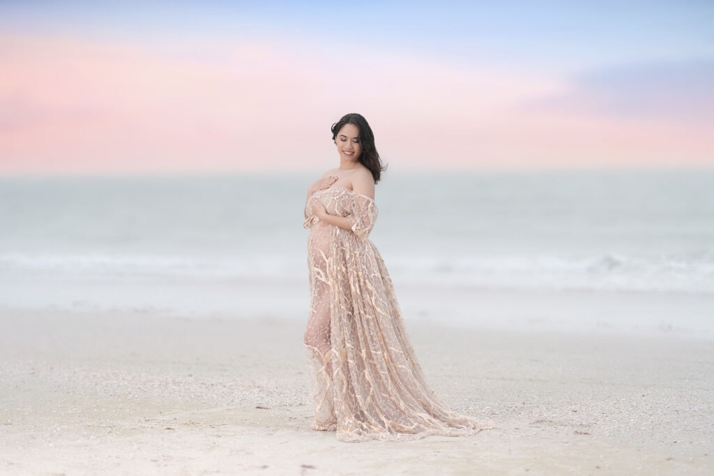 Maternity portrait of woman in a lace gown posed at a beach