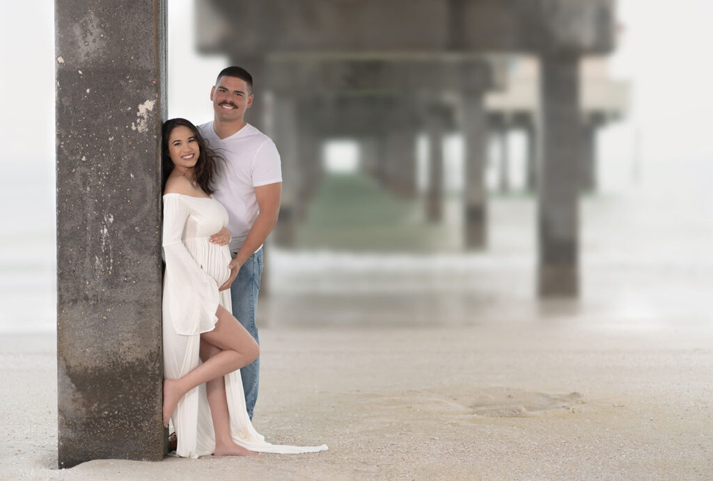 Couples maternity portrait of couple posed under a pier