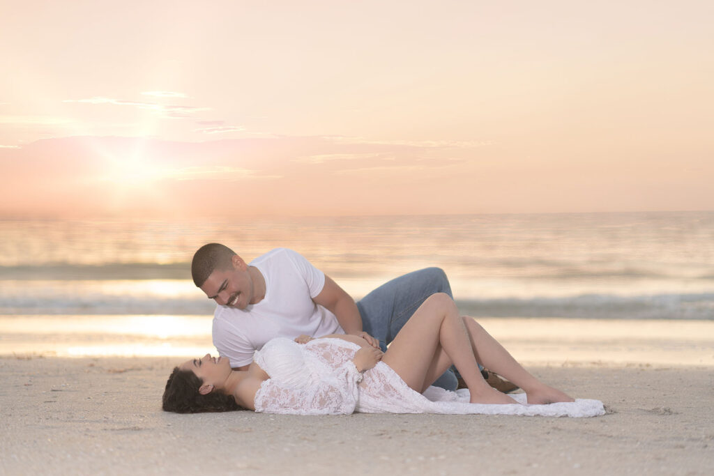 Intimate couples maternity portrait of a couple laying at the beach at sunset
