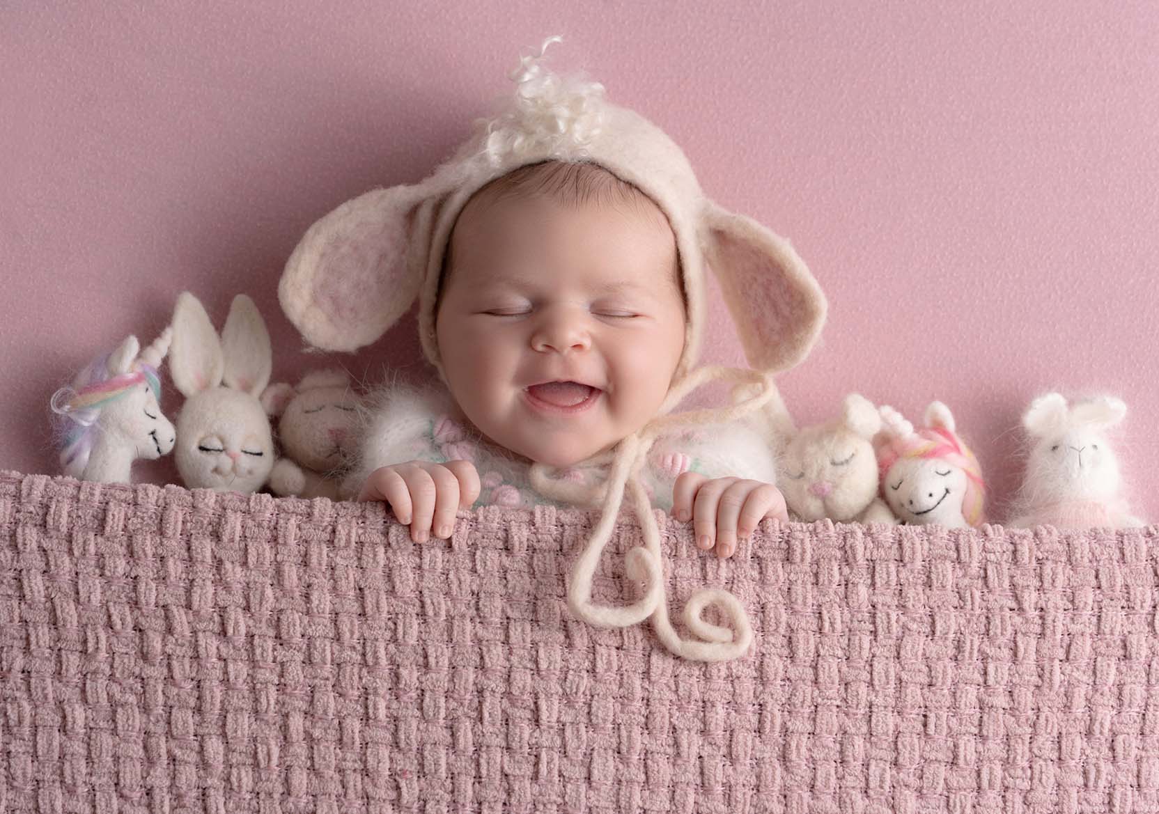 Newborn portrait of baby in a pink set with stuffed animals around them