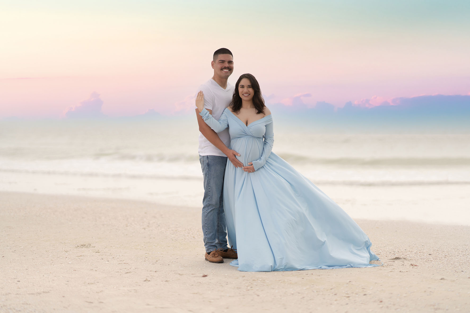 Maternity portrait of couple on a beach where the mother is wearing a flowing pastel blue gown