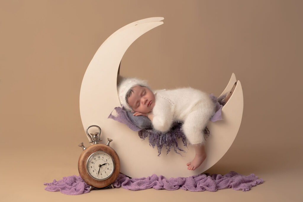 Newborn portrait of baby posed sleeping in a half moon prop