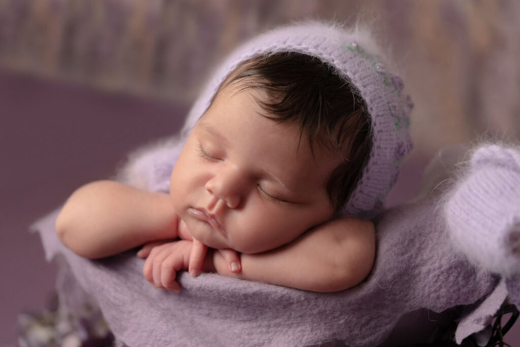 Serene newborn portrait of baby wearing a purple knit head covering sleeping in a pot