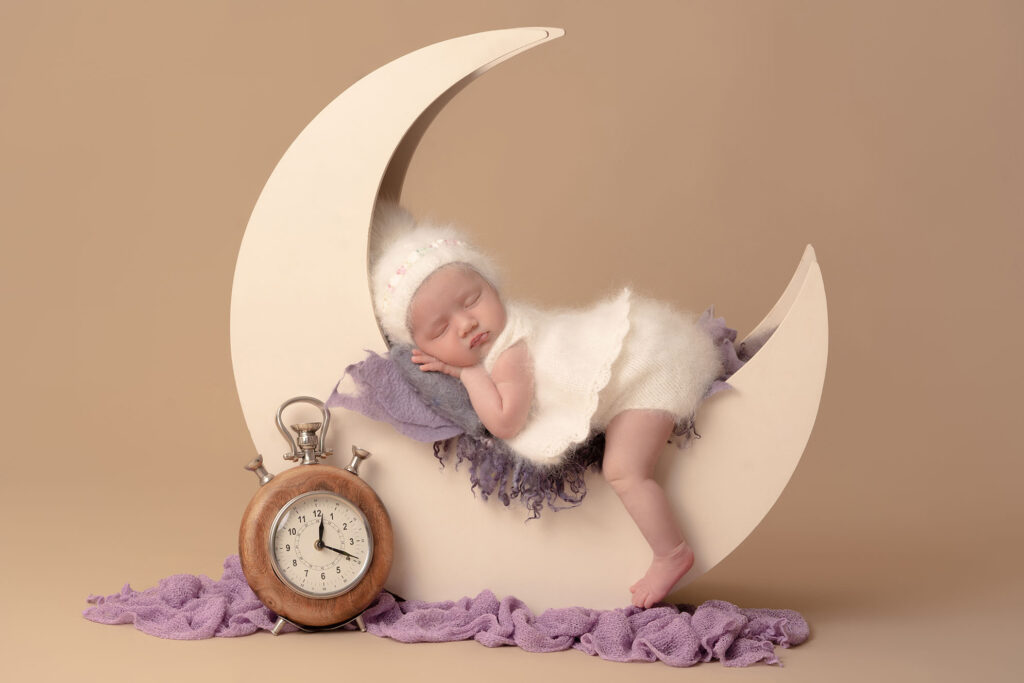Newborn portrait of baby posed sleeping in a half moon prop