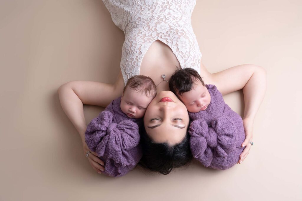 Portrait of mother with bold makeup and her newborn twins wrapped in purple blankets