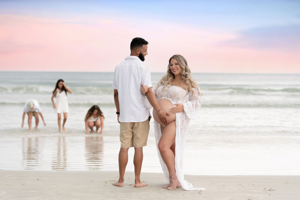 Family portrait of husband holding his wife's pregnant stomach while their kids play in the background