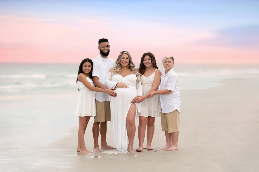 Family portrait of family wearing all neutrals at the beach posed with a sunset in the background