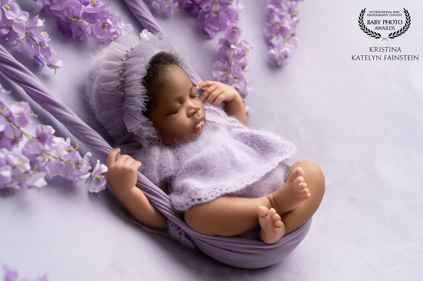 Portrait of newborn in a purple themed set in a swing with flowers around her